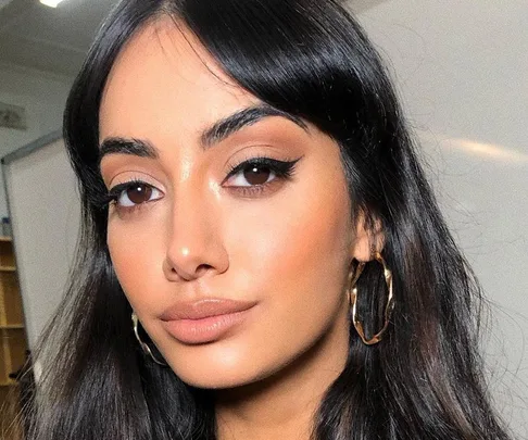 Woman with long, dark hair and curtain bangs, wearing hoop earrings, in a well-lit indoor setting.