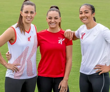 Three athletes in sportswear on a grassy field, smiling and posing with arms around each other.