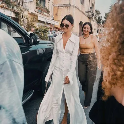 Woman in a white Bec + Bridge dress walking on a street in Italy, accompanied by friends, in a casual and stylish manner.