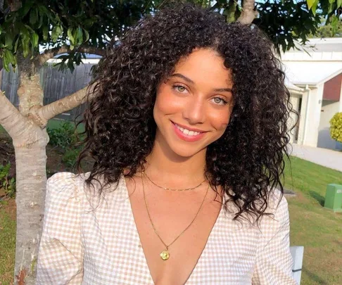 Smiling woman with curly hair in a garden setting.