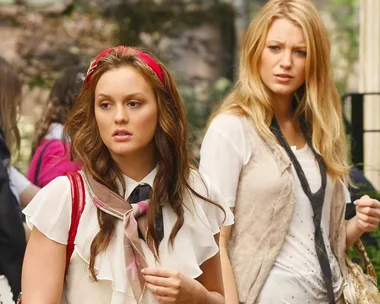 Two women walking outdoors, one with a red headband, the other with long blonde hair, wearing stylish outfits.