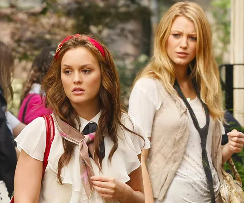 Two women walking outdoors, one with a red headband, the other with long blonde hair, wearing stylish outfits.