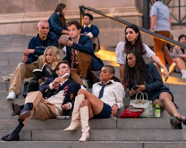 Group of stylish young adults sitting on outdoor steps, engaged in conversation from the "Gossip Girl" reboot.