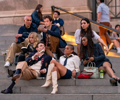 Group of stylish young adults sitting on outdoor steps, engaged in conversation from the "Gossip Girl" reboot.