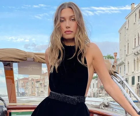 A woman in a black dress poses on a boat with Venetian buildings in the background.