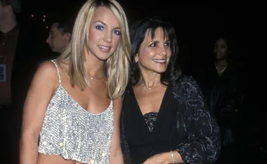 A woman in a sparkly top poses with another woman in a dark outfit at an event, both smiling.