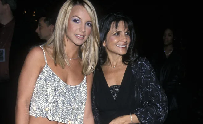 A woman in a sparkly top poses with another woman in a dark outfit at an event, both smiling.