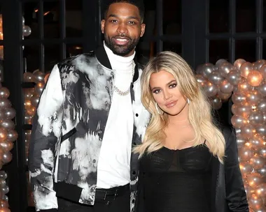 Man and woman posing together at an event with a balloon arch background.