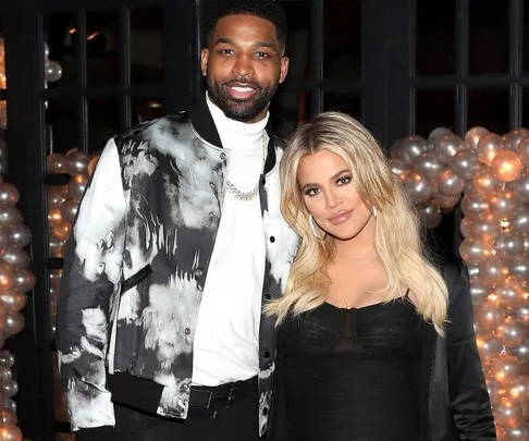 Man and woman posing together at an event with a balloon arch background.