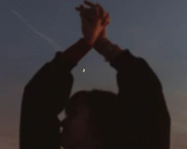 Silhouette of a person with hands raised against a twilight sky and a visible crescent moon.