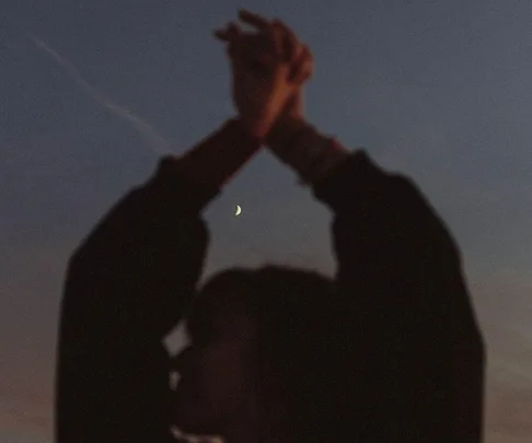 Silhouette of a person with hands raised against a twilight sky and a visible crescent moon.