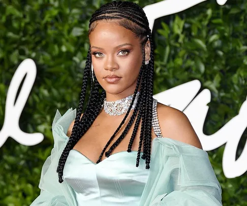 Woman with braided hair in an off-shoulder dress and diamond choker, against a leafy green backdrop.