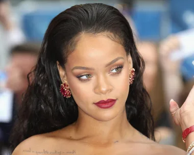 Woman with long dark hair, red lipstick, and red earrings at an event, looking to the side.