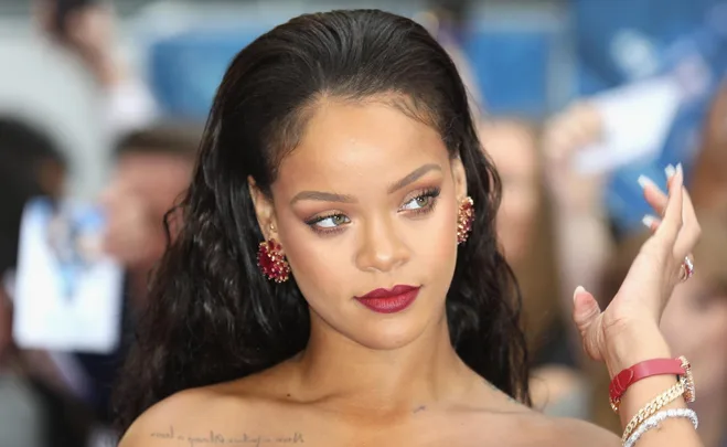 Woman with long dark hair, red lipstick, and red earrings at an event, looking to the side.