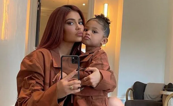 A woman and a young girl in matching brown outfits take a mirror selfie, posing with pouting expressions.