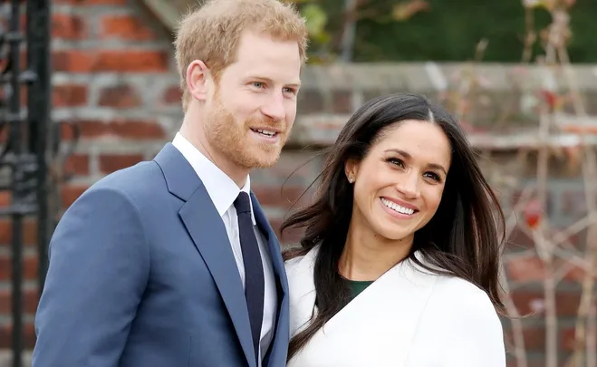 A smiling couple poses outdoors, the man in a blue suit and the woman in a white coat.