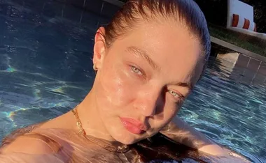 A woman with wet hair is relaxing in a swimming pool, capturing sunlight on her face.