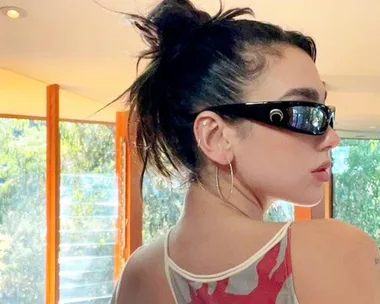 Woman with dark hair in a bun wearing wraparound sunglasses and hoop earrings in a sunlit room.