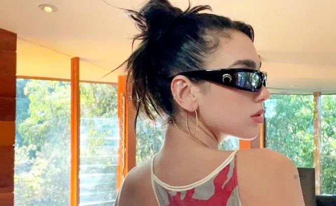 Woman with dark hair in a bun wearing wraparound sunglasses and hoop earrings in a sunlit room.