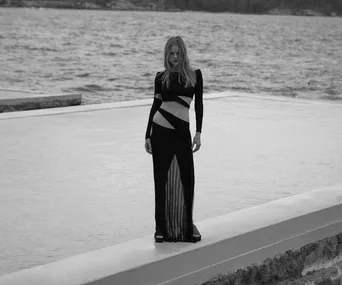 Model in a cutout black dress stands by a seaside pool, showcasing Aya Muse Resort '22 collection.