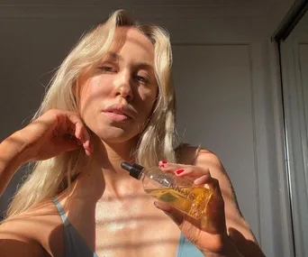 Person holding a bottle of skincare oil, with sunlight highlighting their skin.