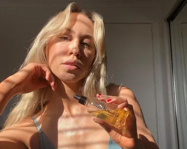 Person holding a bottle of skincare oil, with sunlight highlighting their skin.