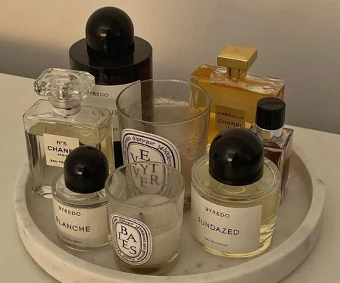 A collection of luxury perfumes, including Chanel and Byredo, arranged on a round tray with candles.