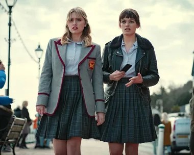 Two young women in school uniforms stand on a street, appearing concerned, from the show "Sex Education."