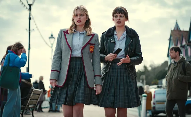 Two young women in school uniforms stand on a street, appearing concerned, from the show "Sex Education."