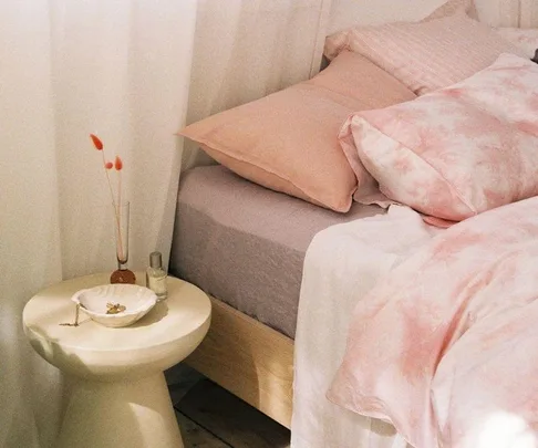 Cozy bedroom with pink and white bedding, bedside table, and decorative items in soft lighting.