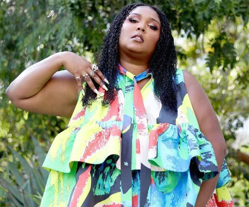 Woman in colorful dress stands confidently in front of leafy background.