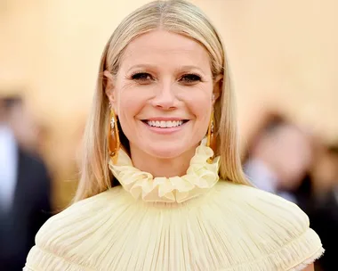 A person smiling in a ruffled yellow dress, with long hair, at a formal event.