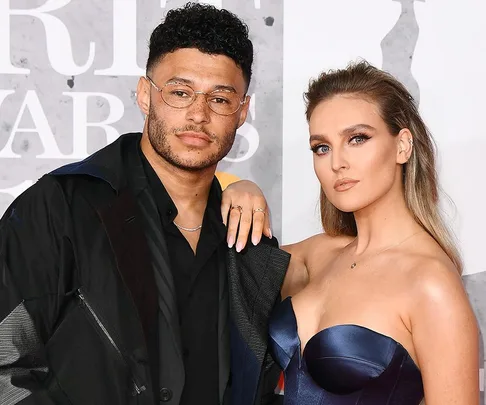 Couple posing on a red carpet, dressed formally, with a neutral backdrop.