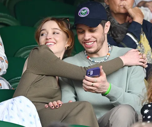 A couple smiling and embracing while sitting in a stadium, with one person holding a phone.