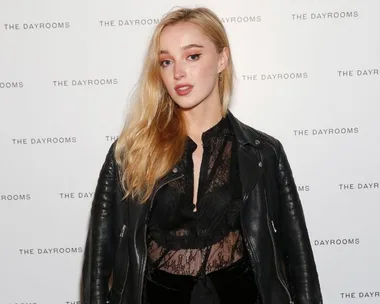 A person in a black lace top and leather jacket at an event with "THE DAYROOMS" logo on the background.