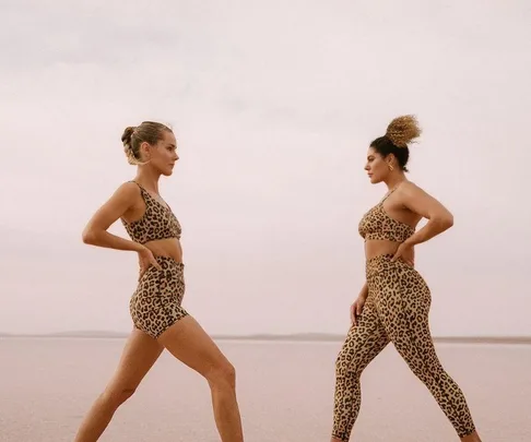 Two women in leopard print activewear walking towards each other on a sandy landscape.