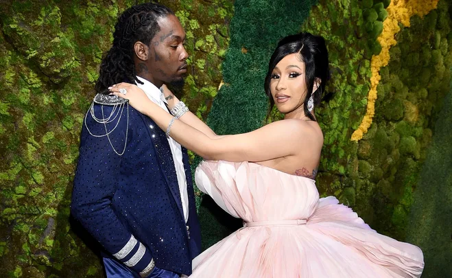 Cardi B in a pink gown embracing Offset in a blue suit against a green, leafy background.