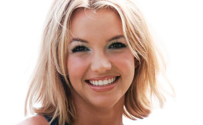 Close-up of a young woman with blonde hair smiling against a plain white background.