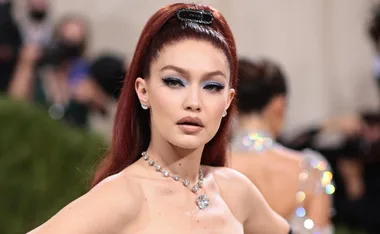 Gigi Hadid at the Met Gala, wearing a strapless dress and diamond necklace with sleek red hair styled upward.