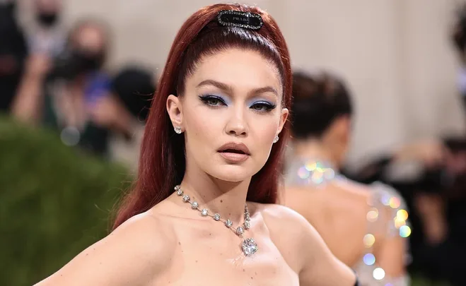 Gigi Hadid at the Met Gala, wearing a strapless dress and diamond necklace with sleek red hair styled upward.