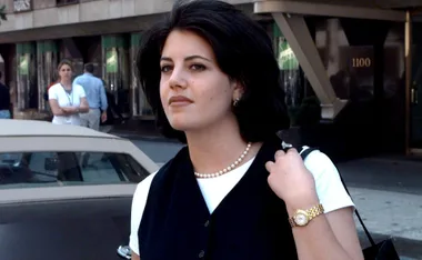 Young woman with dark hair wearing a pearl necklace, standing outdoors on a city street.