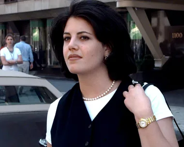 Young woman with dark hair wearing a pearl necklace, standing outdoors on a city street.