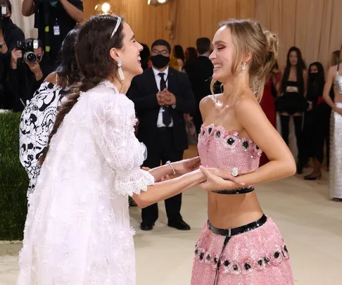 Two women smiling and holding hands on the Met Gala red carpet, dressed in elegant embellished outfits.