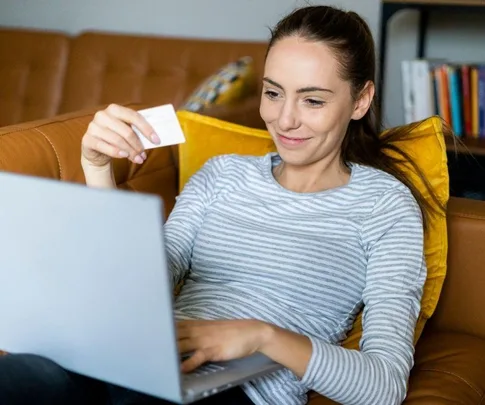 Woman holding a credit card, shopping online with a laptop on a couch.