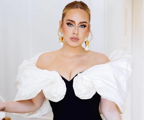 A person wearing a black dress with white, ruffled, off-shoulder sleeves, elegant makeup, and large earrings.