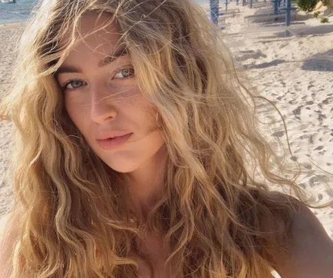 Woman with wavy blonde hair on a sunny beach.