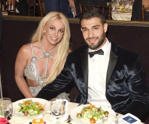 A couple seated at a formal event, smiling, with salads on the table in front of them.