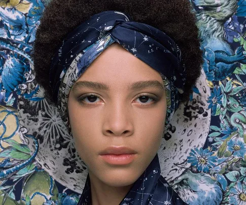 Model wearing a blue patterned headscarf with floral background in Dior campaign.