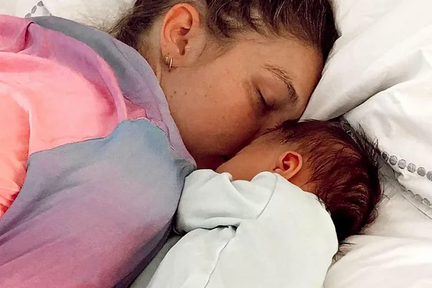 Mother and baby snuggle on a bed, wrapped in colorful blankets.