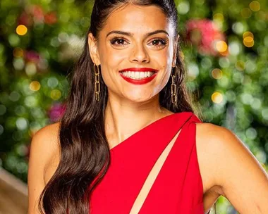 Smiling woman in a red dress with long hair and gold earrings, against a blurred garden background.